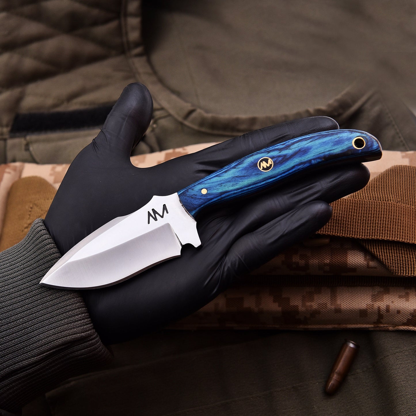 Knife with blue handle held in a black gloved hand against a camouflage background