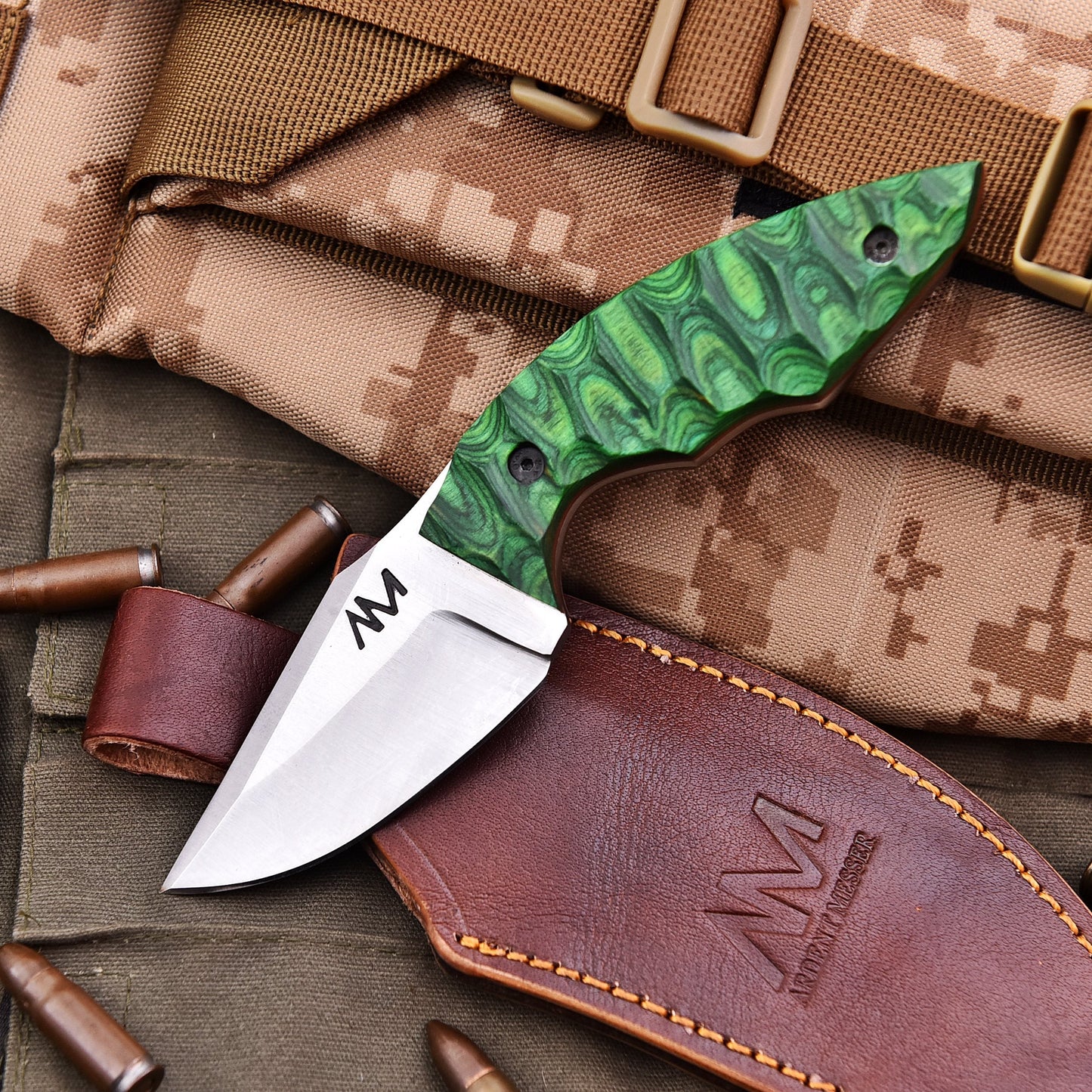 Folding knife with green patterned handle on camouflage fabric and leather pouch