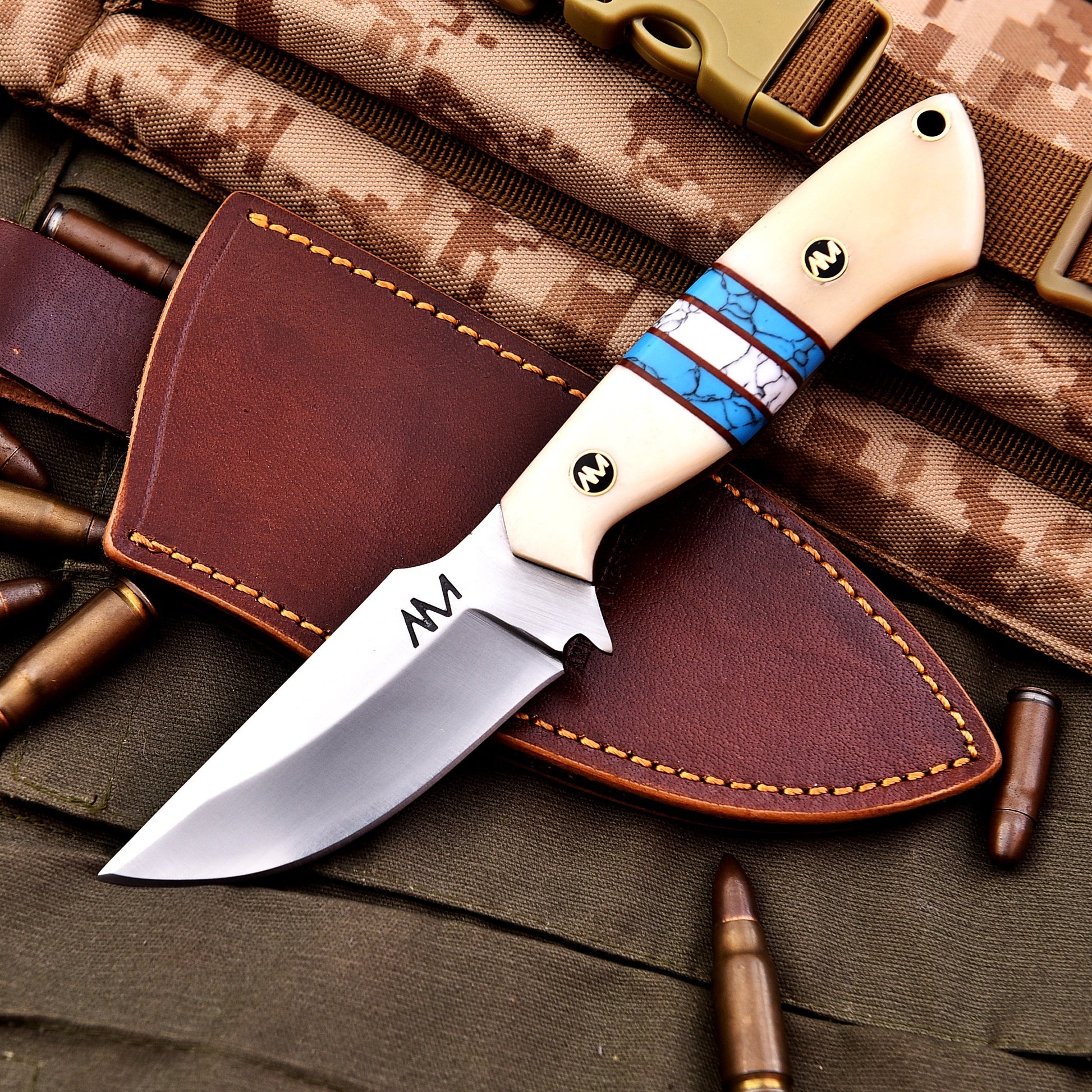Knife with American flag handle on a leather sheath, surrounded by camouflage fabric and bullets.