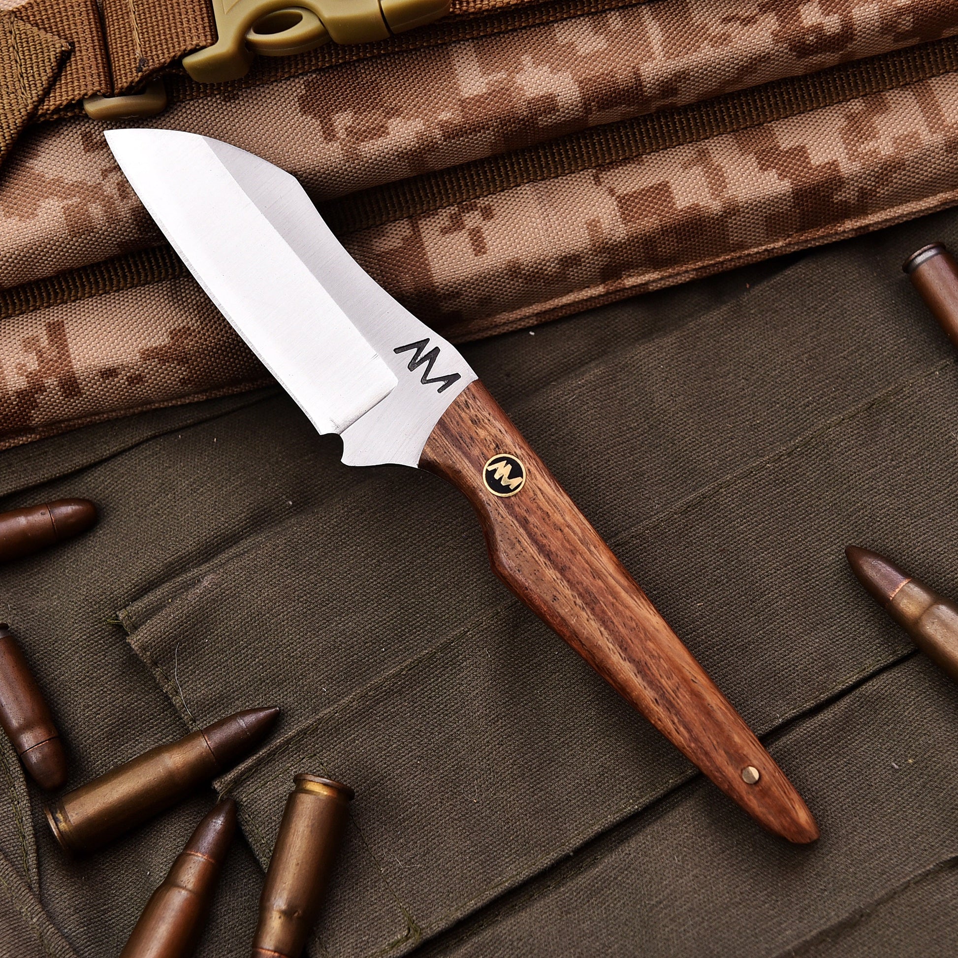 Knife with wooden handle and metal blade on camouflage fabric with bullets