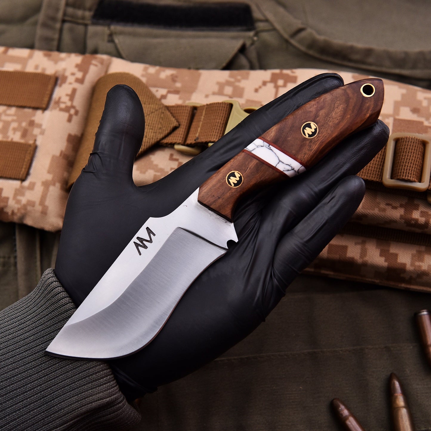 Knife with wooden handle held by a gloved hand on camouflage background