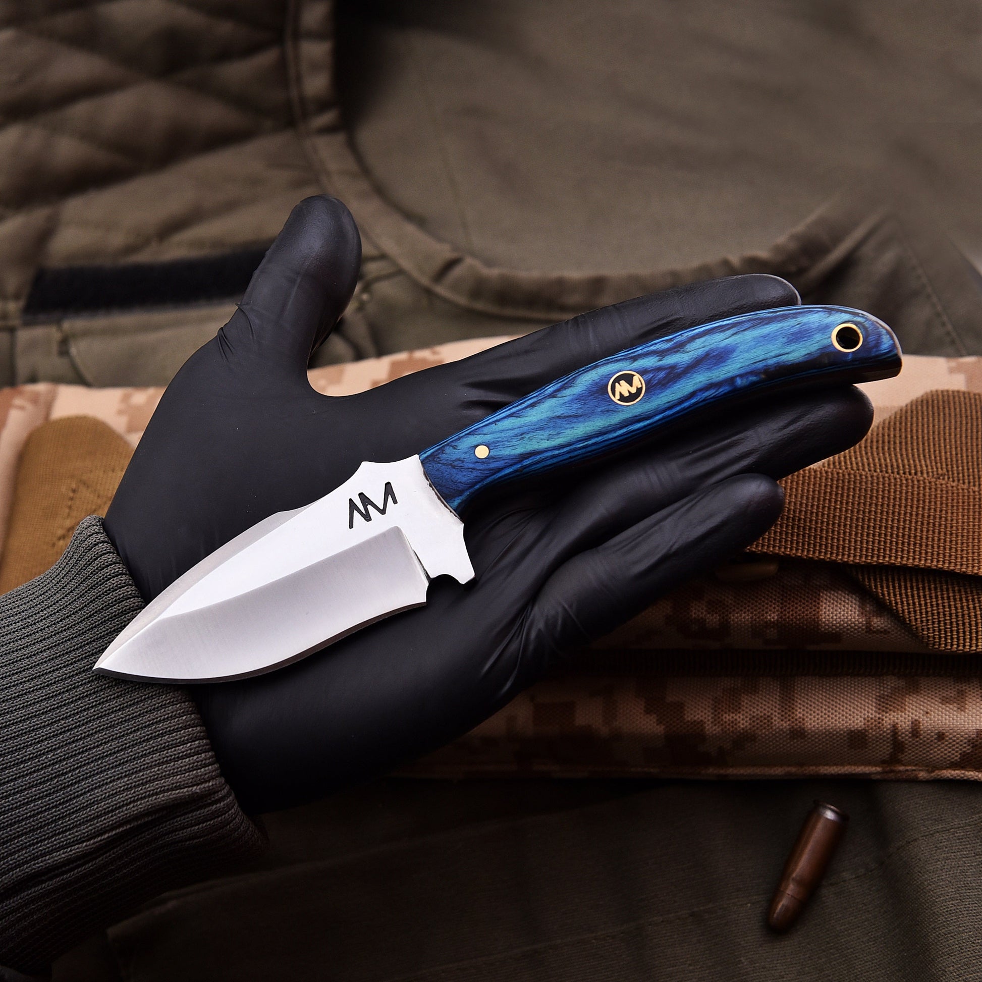 Knife with blue handle held in a black gloved hand against a camouflage background