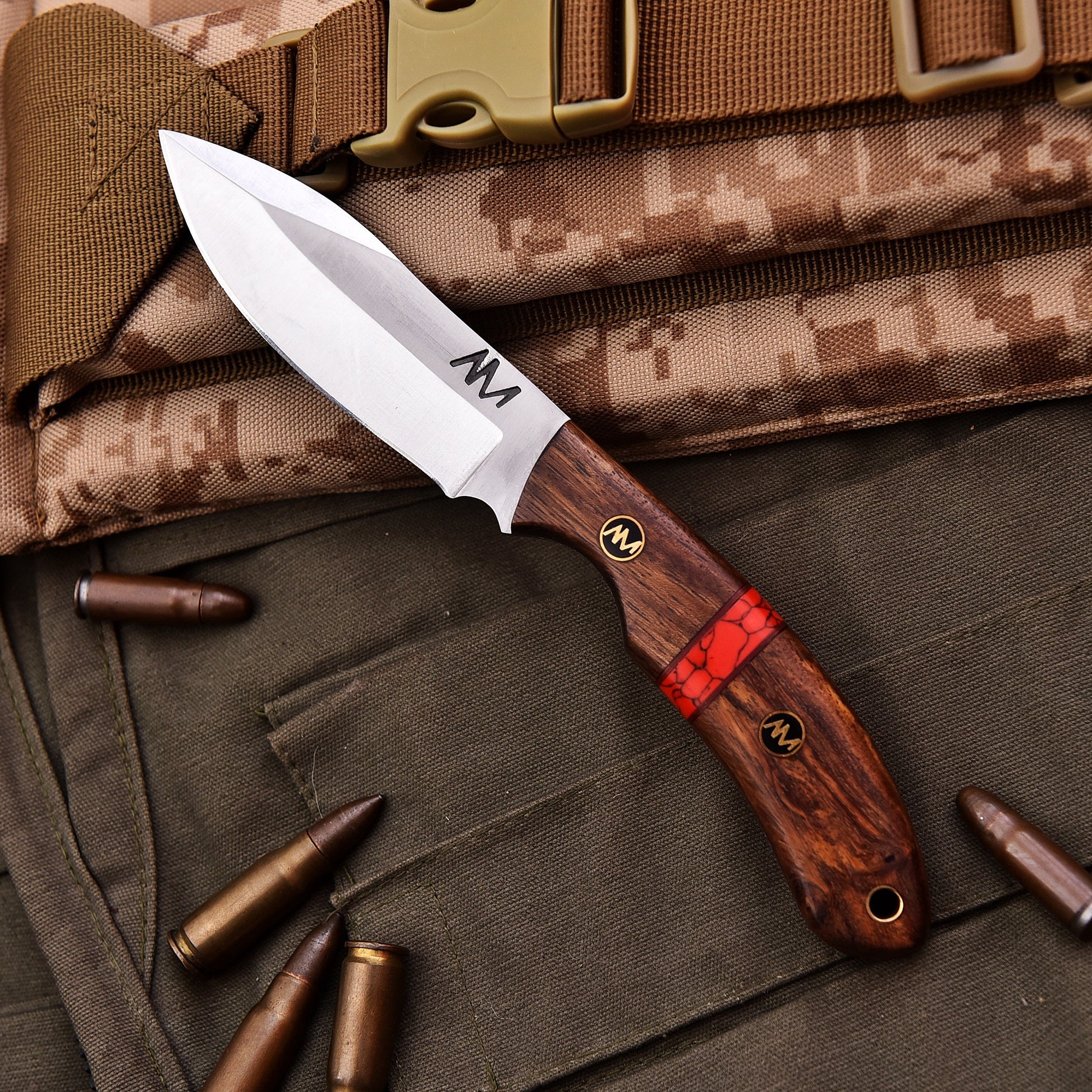 Tactical knife with wooden handle and red accent on camouflage gear
