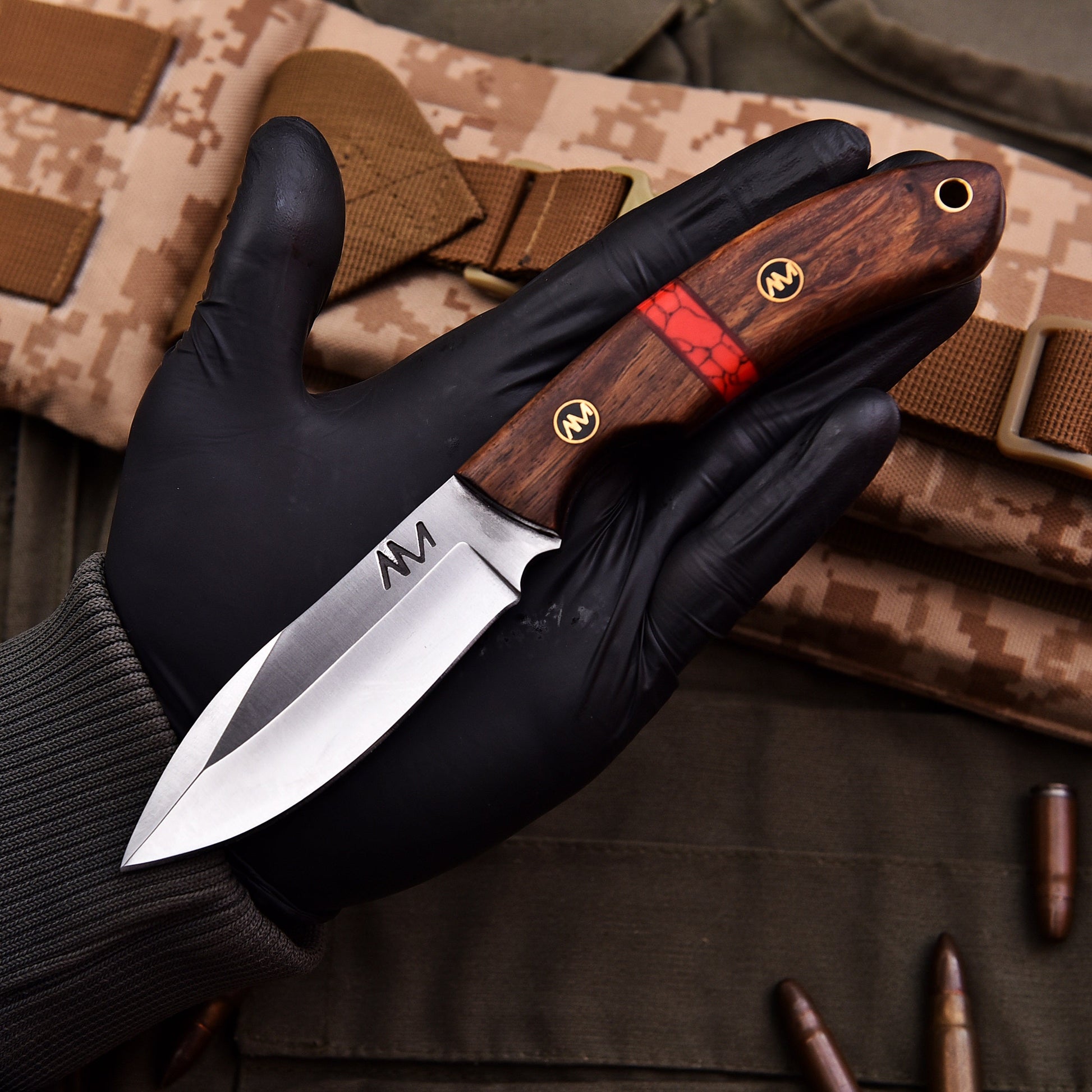 Knife with wooden handle held by a gloved hand on camouflage background