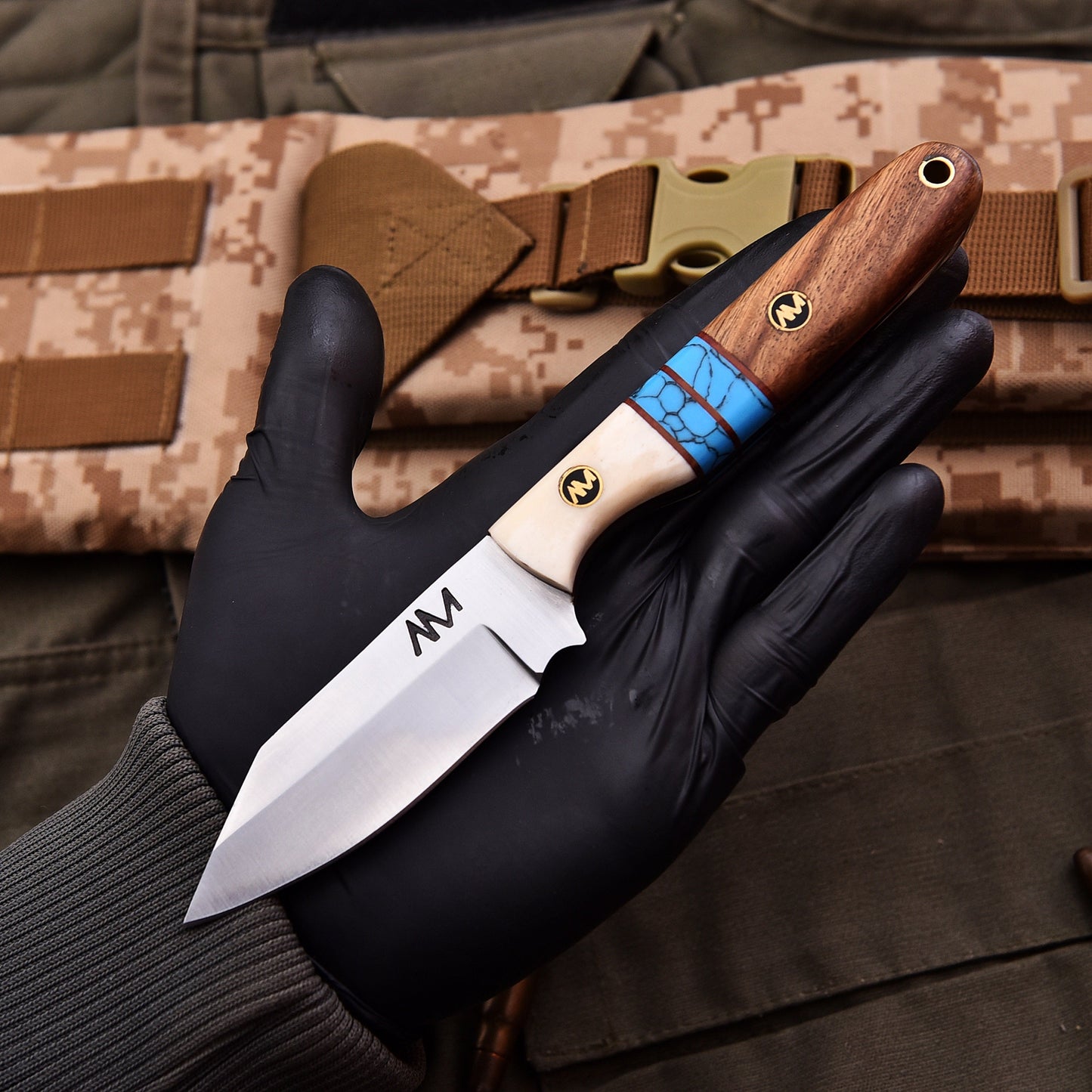 Knife with wooden handle and blue accent held by a gloved hand, with camouflage background