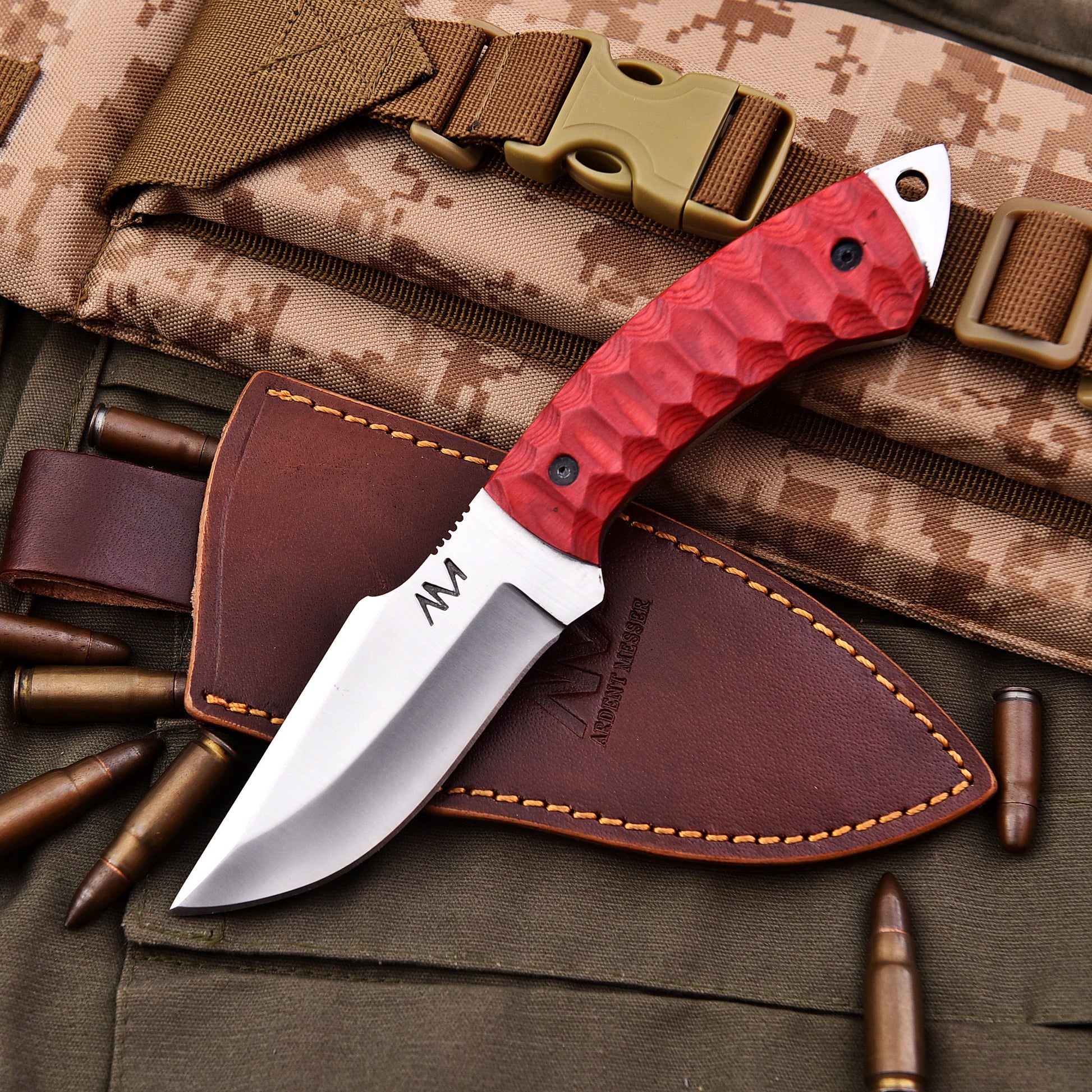 Red-handled knife with leather sheath on camouflage background