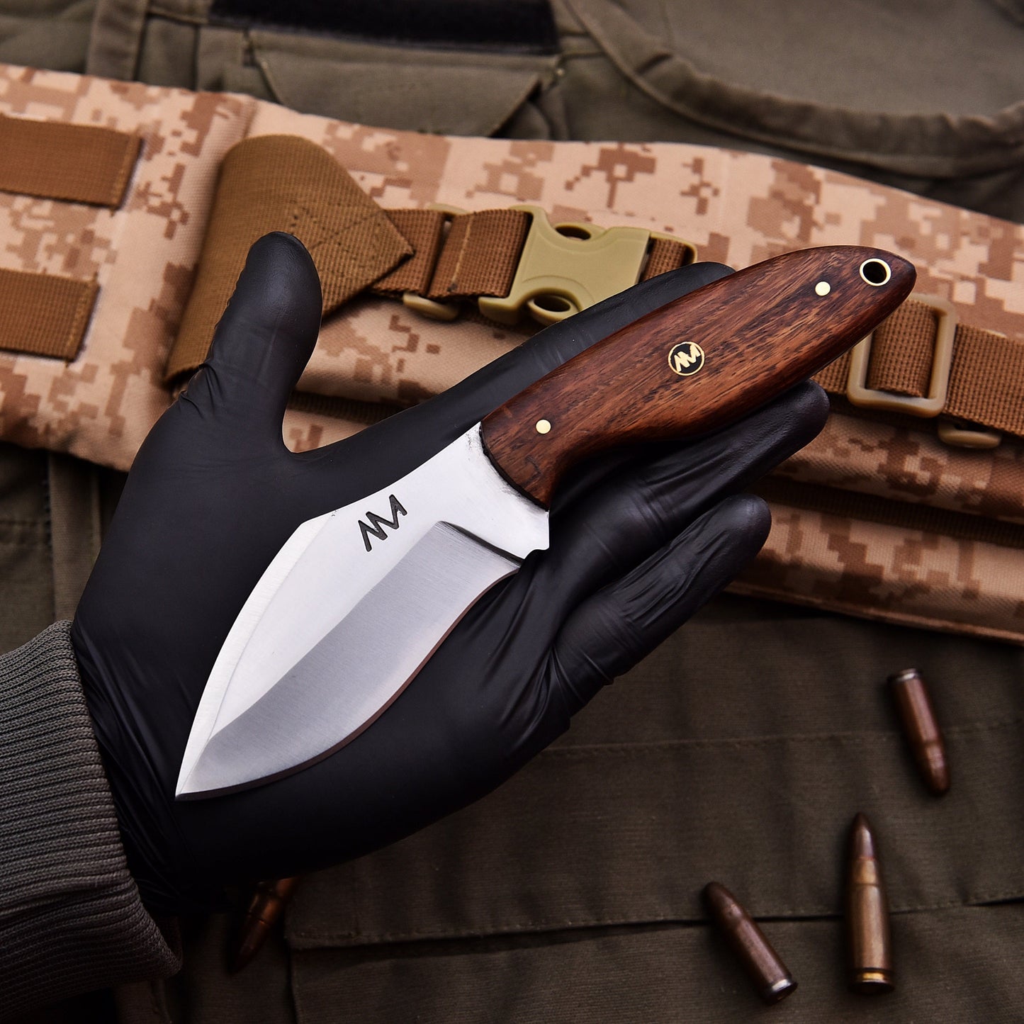 Hand holding a knife with a wooden handle on camouflage fabric