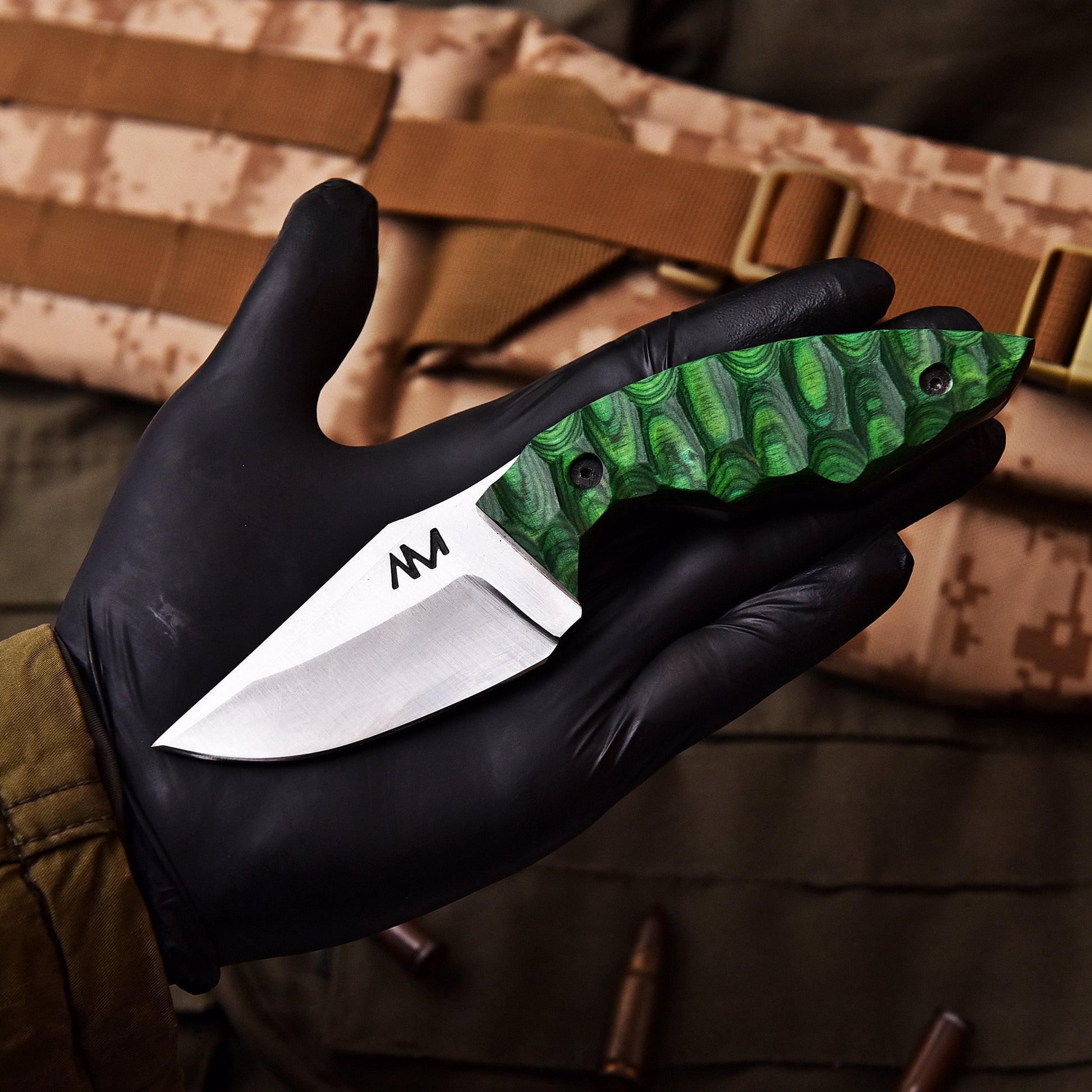 Green folding knife held in a black gloved hand with camouflage background
