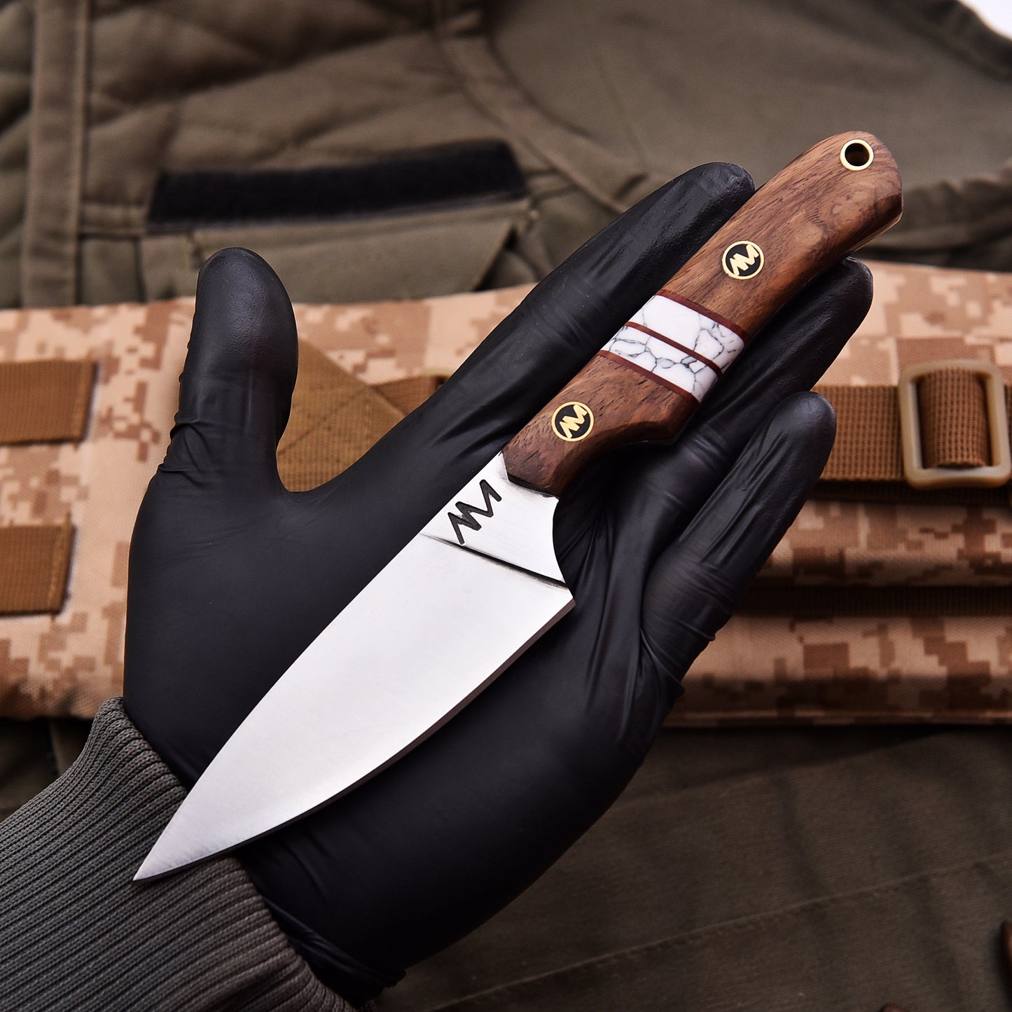 Hand holding a knife with a wooden handle against a camouflage background