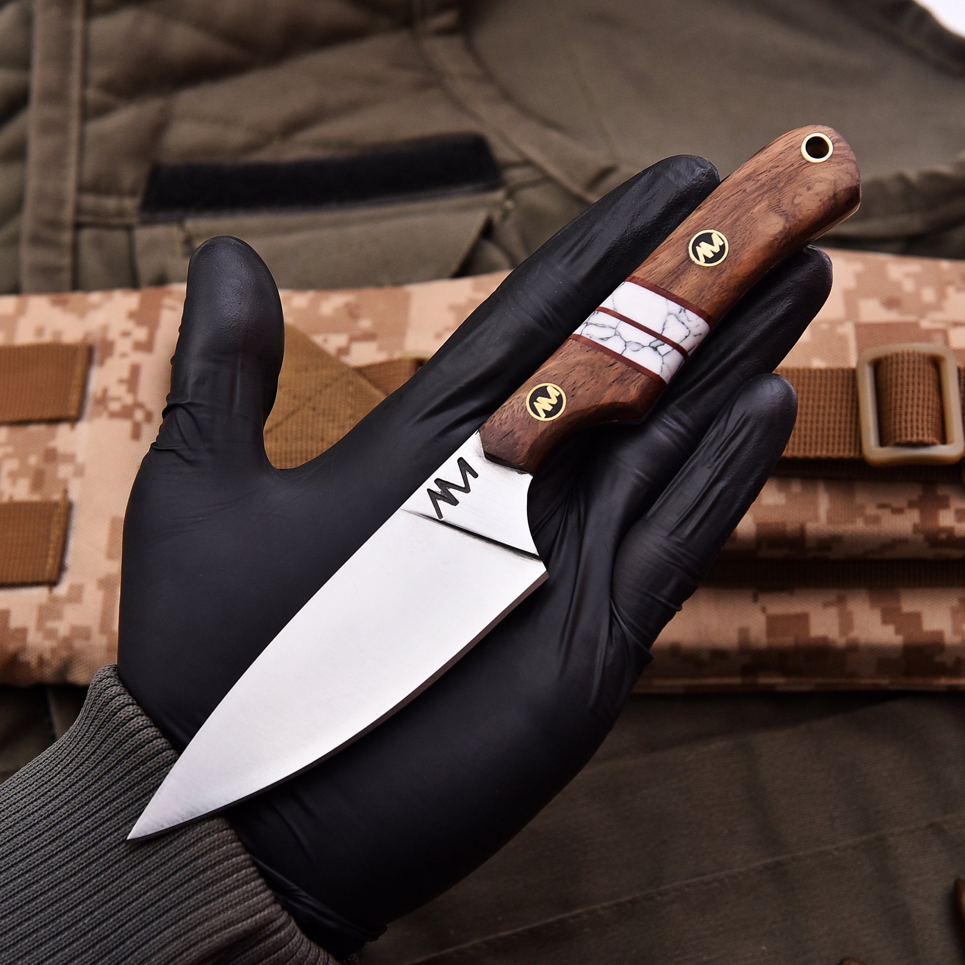 Hand holding a knife with a wooden handle against a camouflage background