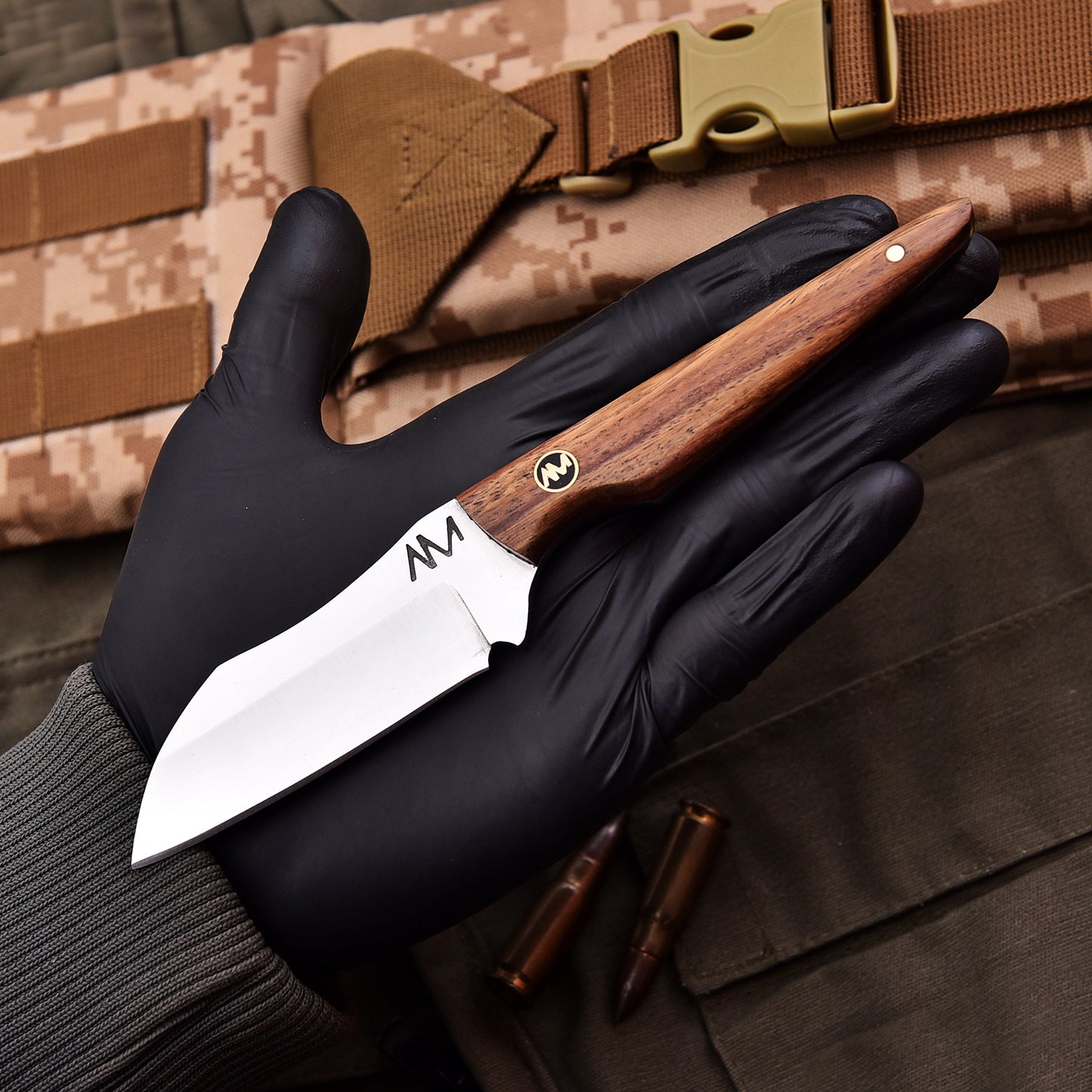 Knife with wooden handle held by a gloved hand, camouflage background