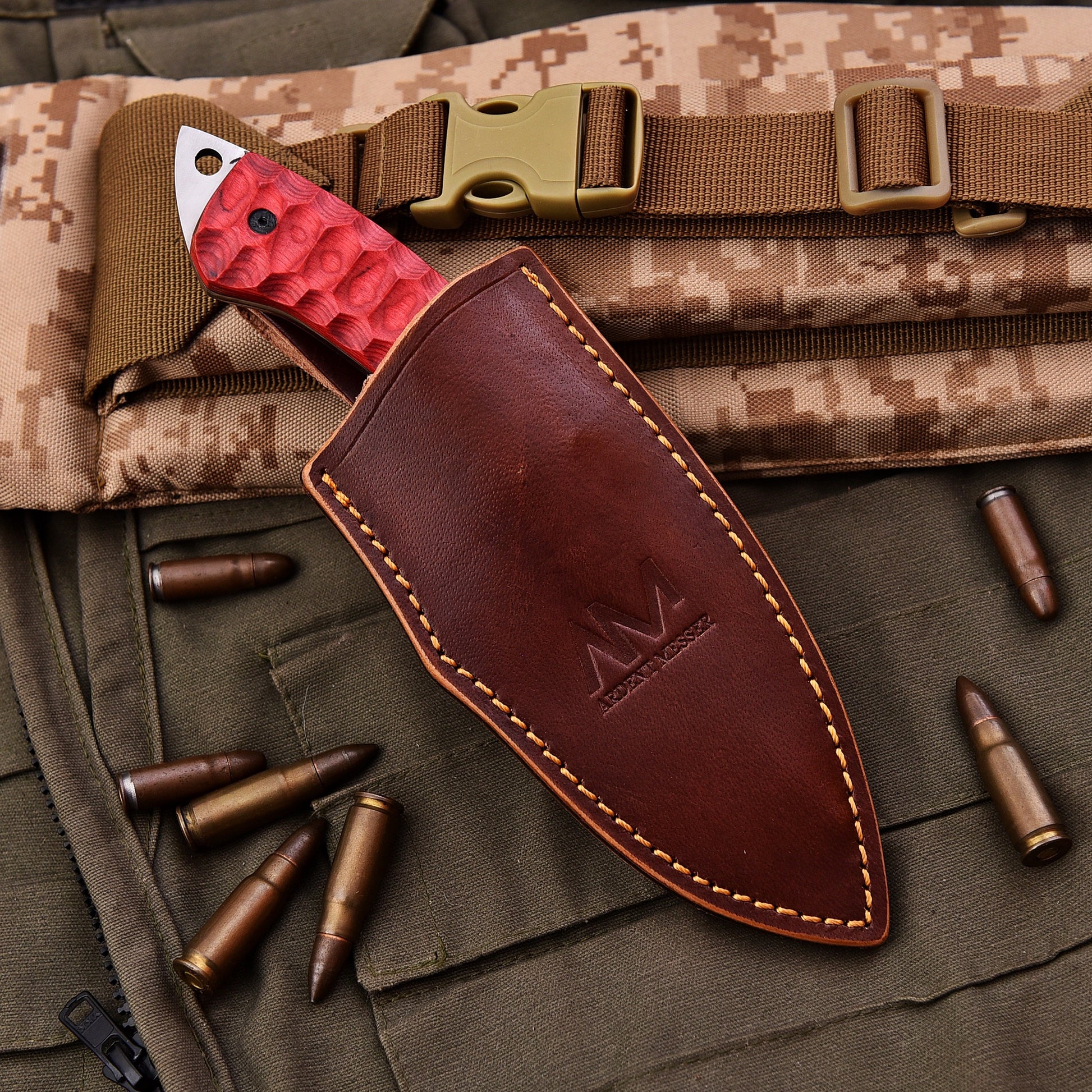 Tactical knife with red blade and brown sheath on camouflage fabric with bullets
