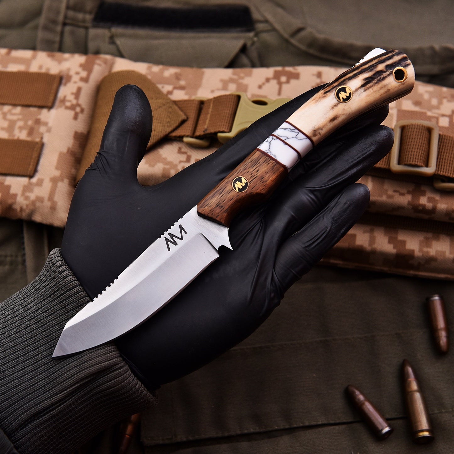 Hand holding a knife with a wooden handle over camouflage fabric and ammunition.